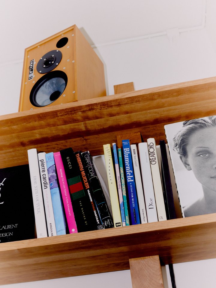 Fashion books under a speaker on a cherry-wood shelf at Simone